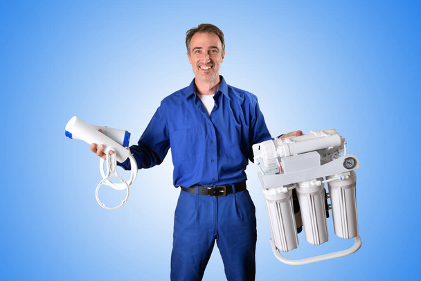 Domestic water treatment technician with reverse osmosis equipment and filter with hand making ok gesture and blue isolated background. Front view. Horizontal composition. - Фото, зображення