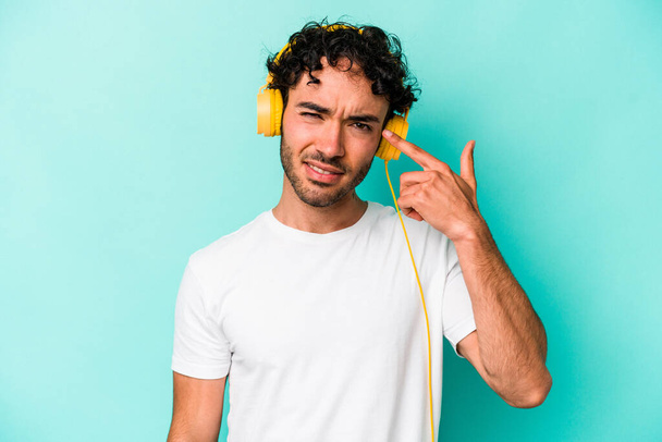 Young caucasian man listening to music isolated on blue background showing a disappointment gesture with forefinger. - Photo, Image