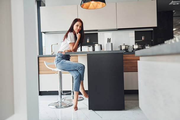 Young beautiful brunette in casual clothes sits in kitchen with fresh drink at morning time. - Photo, Image