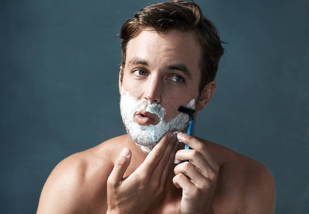 Keeping a clean shave. Cropped shot of a handsome young man shaving against a grey background. - 写真・画像