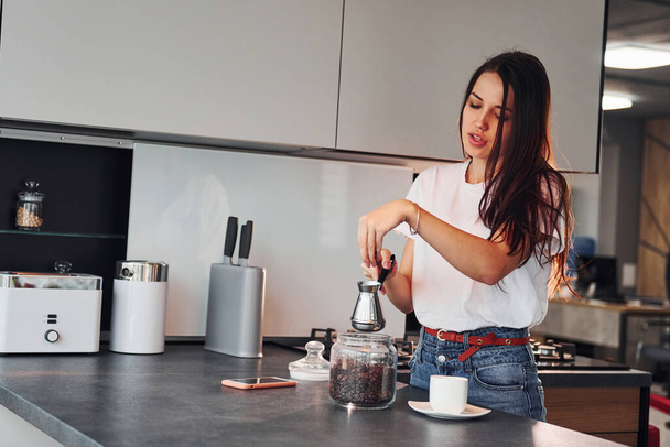 Young beautiful brunette in casual clothes preparing coffee in kitchen at daytime. - Foto, Imagen