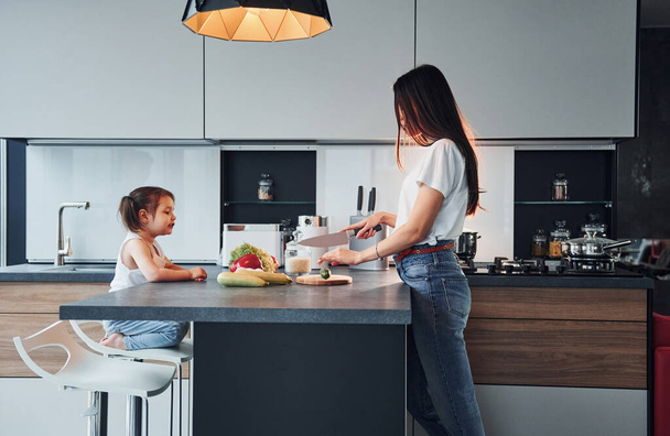 Side view of mother that with her little daughter preparing food indoors in kitchen. - 写真・画像