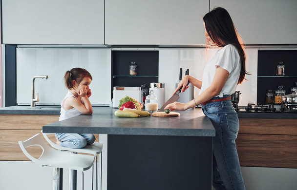 Side view of mother that with her little daughter preparing food indoors in kitchen. - Φωτογραφία, εικόνα