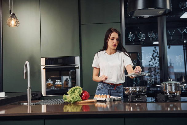 Preparing food by using vegetables and healthy products. Young beautiful brunette in casual clothes indoors in kitchen at daytime. - Foto, Imagen