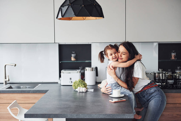 Mother with her little daughter embracing each other indoors in kitchen. - Photo, Image