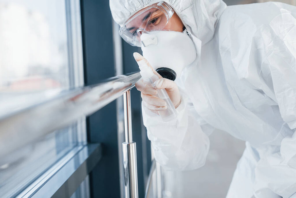 Female doctor scientist in lab coat, defensive eyewear and mask standing indoors with antibacterial spray. - Foto, imagen