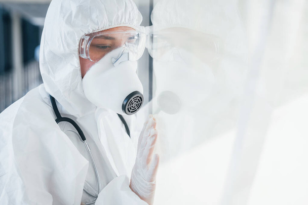 Feels bad and sick. Female doctor scientist in lab coat, defensive eyewear and mask standing indoors. - Foto, Imagem