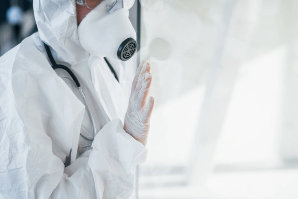 Feels bad and sick. Female doctor scientist in lab coat, defensive eyewear and mask standing indoors. - Photo, image