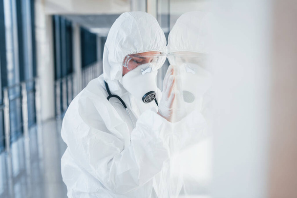 Feels bad and sick. Female doctor scientist in lab coat, defensive eyewear and mask standing indoors. - Fotoğraf, Görsel