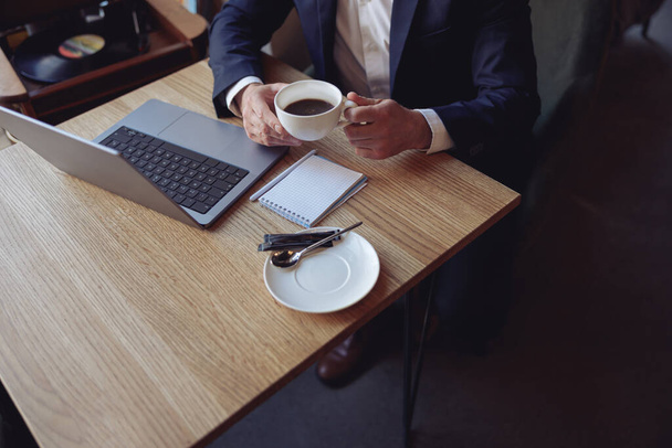 Cup of coffee in male hands of businessman sitting at table with laptop. Business concept. - Photo, image