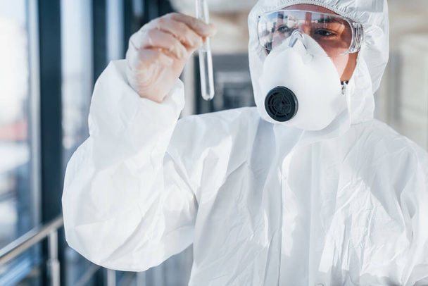 With test tube in hand. Female doctor scientist in lab coat, defensive eyewear and mask standing indoors. - Foto, Bild