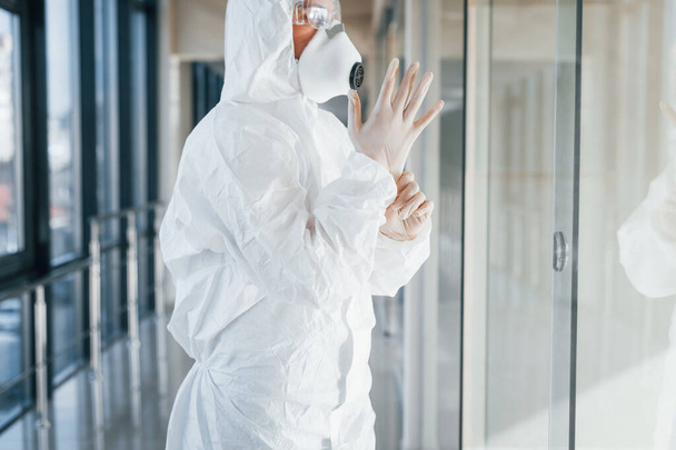 Female doctor scientist in lab coat, defensive eyewear and mask standing indoors and wearing gloves. - Photo, image