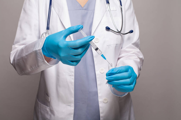 Медичний працівник руки в блакитних медичних рукавичках набирає вакцину в шприц крупним планом
 - Фото, зображення