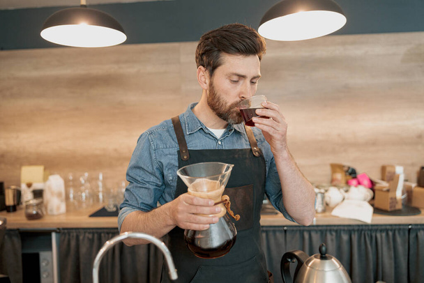 Barista tasting a freshly brewed filter coffee standing behind counter - 写真・画像