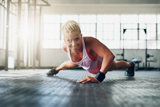 Excuses dont burn calories. Shot of a young attractive woman doing push ups with one hand at the gym. - Fotoğraf, Görsel