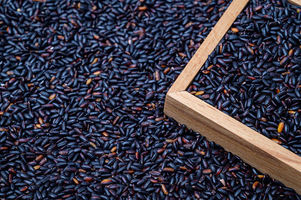 A background with black rice stacked and a wooden bowl containing black rice. - Foto, Bild