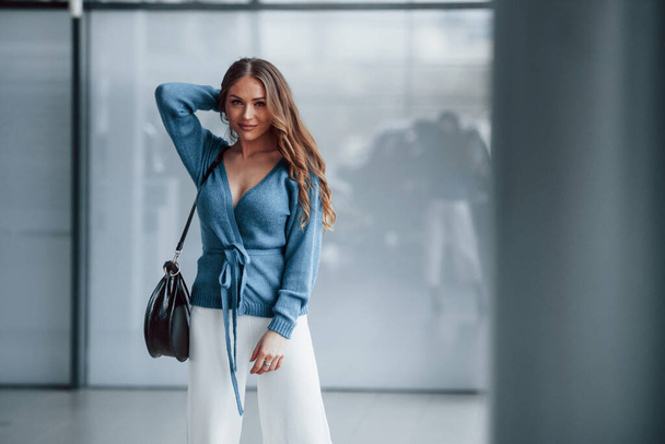 Attractive woman in blue shirt and white pants indoors posing for a camera. In airport or car shop. - Foto, Imagem