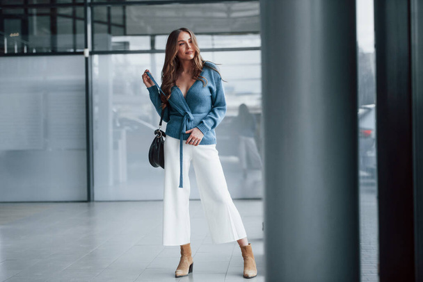 Attractive woman in blue shirt and white pants indoors posing for a camera. In airport or car shop. - Fotografie, Obrázek