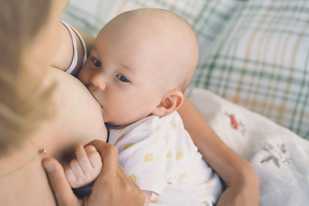 Baby eating mother's milk. Mother breastfeeding baby. Woman breast feeding her newborn baby. Concept of lactation infant, postpartum period, natural motherhood. Close-up photo - 写真・画像