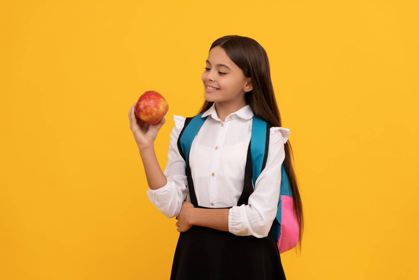 Feliz sonrisa del niño sosteniendo manzana y la bolsa de la escuela fondo amarillo, volver a la escuela - Foto, imagen