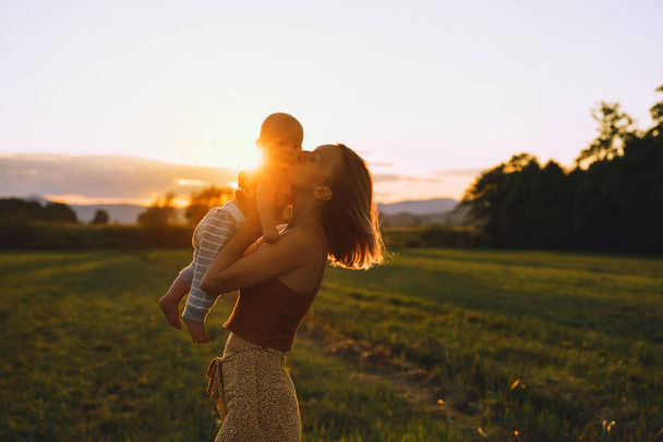 Loving mother and baby at sunset. Beautiful woman and small child in nature background. Concept of natural motherhood. Happy healthy family at summer outdoors. Positive human emotions and feelings. - Fotoğraf, Görsel