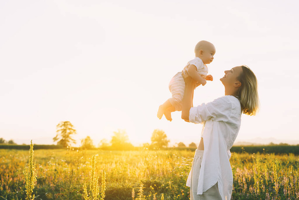 Loving mother and baby at sunset. Beautiful woman and small child in nature background. Concept of natural motherhood. Happy healthy family at summer outdoors. Positive human emotions and feelings. - Zdjęcie, obraz
