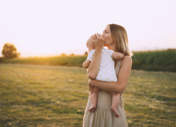Loving mother and baby at sunset. Beautiful woman and small child in nature background. Concept of natural motherhood. Happy healthy family at summer outdoors. Positive human emotions and feelings. - Foto, Bild