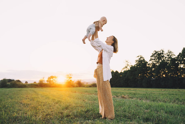 Loving mother and baby at sunset. Beautiful woman and small child in nature background. Concept of natural motherhood. Happy healthy family at summer outdoors. Positive human emotions and feelings. - 写真・画像