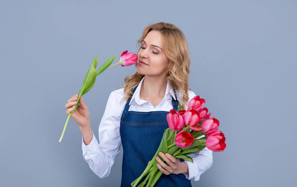 chica feliz en delantal con flores de tulipán de primavera sobre fondo gris - Foto, Imagen