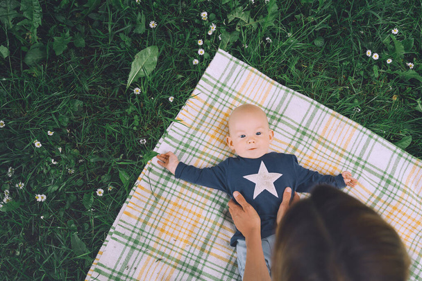 Cute happy baby lying on blanket on green grass at summer outdoors. 3 months old barefoot baby on nature. Family and childhood concept of  eco sustainable lifestyle. - Fotografie, Obrázek