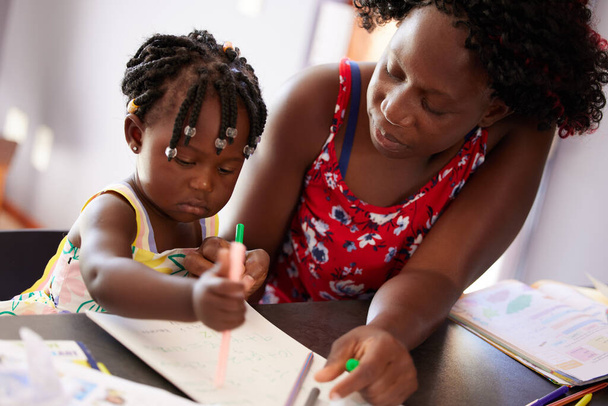 Meiner Tochter dabei zu helfen, auf die beste Weise zu lernen. Aufnahme einer Mutter, die Zeit mit ihrer Tochter verbringt, während sie ein Buch malt. - Foto, Bild