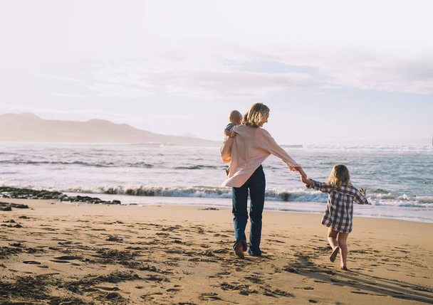 Mother with children playing and having fun together on beach ocean. Happy family outdoors. Mom and kids at summer on nature. Positive human emotions and feelings. Family holiday on sea coast. - Photo, image