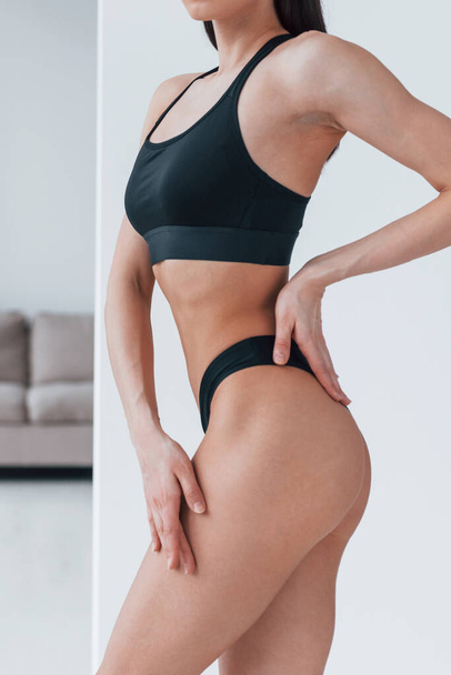 Slender woman in black fitness underwear standing indoors in room at daytime. - Photo, Image