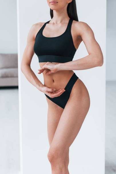 Slender woman in black fitness underwear standing indoors in room at daytime. - Fotó, kép