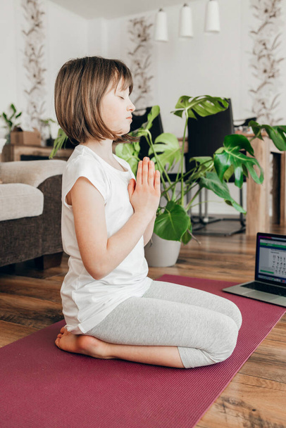 Egy lány, aki otthon jógázik egy sportszőnyegen jógázni. Meditáció és pihenés. Érzelmek kezelése. Jógapózok gyerekeknek - Fotó, kép