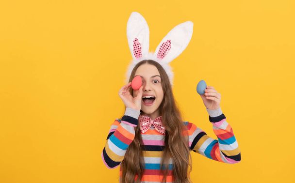 niño feliz en orejas de conejo y pajarita sostienen huevos de Pascua sobre fondo amarillo - Foto, imagen