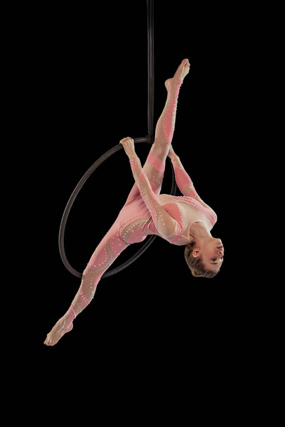 Portrait of young flexible girl, professional air gymnast performing, training isolated over black studio background. Twine position - Fotó, kép
