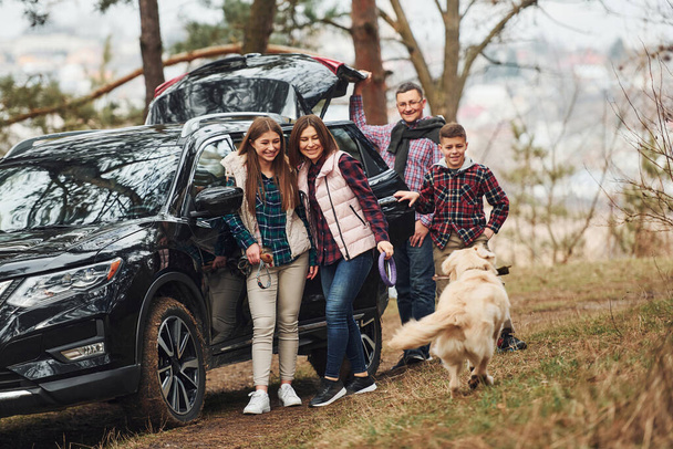 Happy family have fun with their dog near modern car outdoors in forest. - Valokuva, kuva