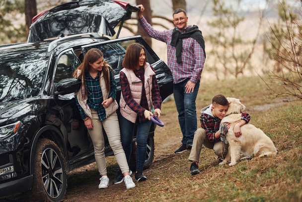 Happy family have fun with their dog near modern car outdoors in forest. - Photo, Image