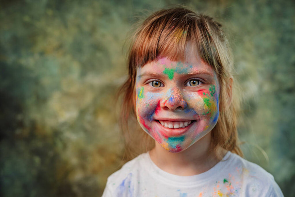 Cara de niña cubierta de colores holi. Retrato de niño feliz sonriente con pinturas colotful en la piel. - Foto, Imagen