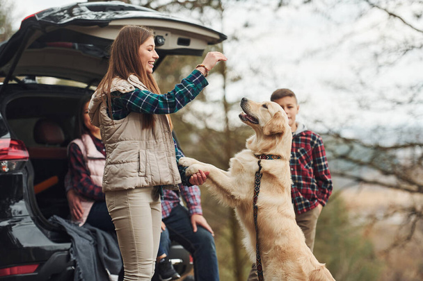 Happy family have fun with their dog near modern car outdoors in forest. - 写真・画像