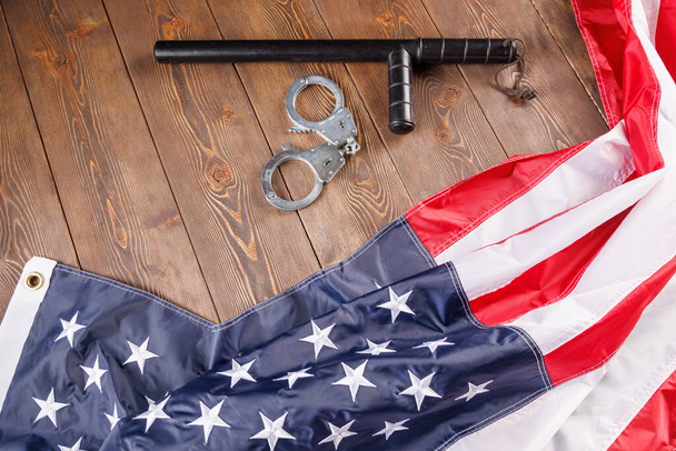 Срібні металеві наручники та поліцейська нічка біля прапора США на дерев'яній поверхні. - Фото, зображення