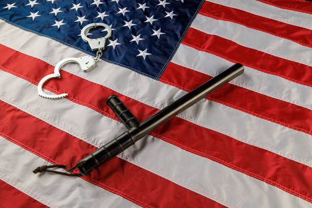 silver metal handcuffs and police nightstick over US flag on flat surface - Foto, immagini