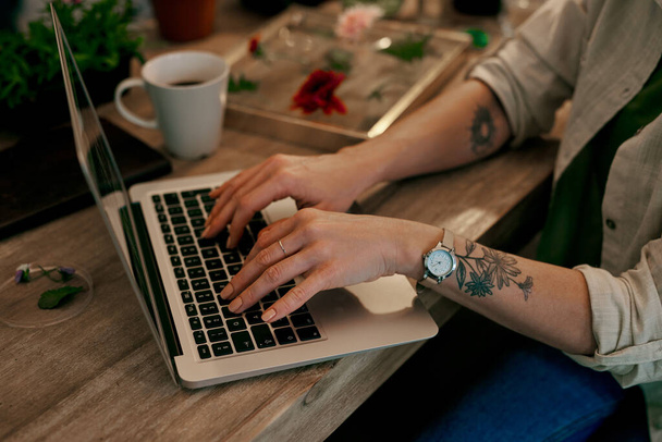 Ik maakte van mijn passie een succesvol bedrijf. Gehakte foto van een onherkenbare bloemist die werkt op een laptop in haar winkel. - Foto, afbeelding