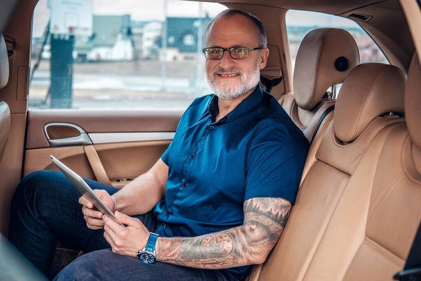 Joyful elderly entrepreneur using tablet inside of car - Valokuva, kuva