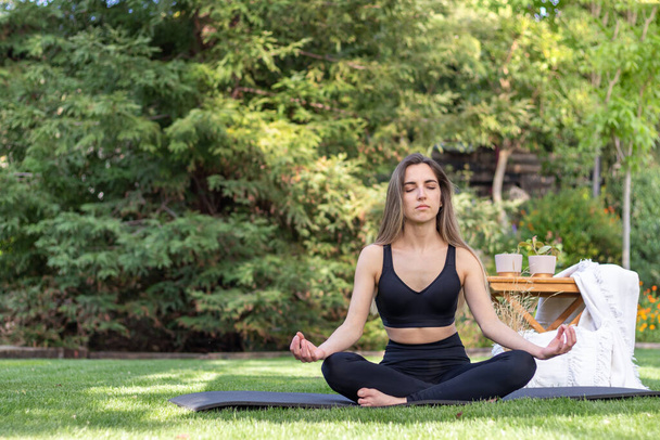 Young beautiful woman in activewear meditating in yoga pose in nature landscape with afternoon light in summer - Фото, изображение