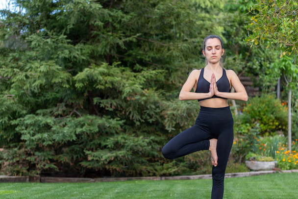 Zdolna młoda kobieta praktykująca jogę i medytację z zamkniętymi oczami w otoczeniu natury w czarnym stroju sportowym - Zdjęcie, obraz