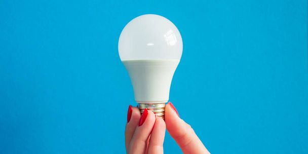 lamp in a woman's hand. female fingers holding LED lamp. idea. white lamp. red manicure. blue background. Horizontal image. Banner for insertion into site. - Foto, Imagen