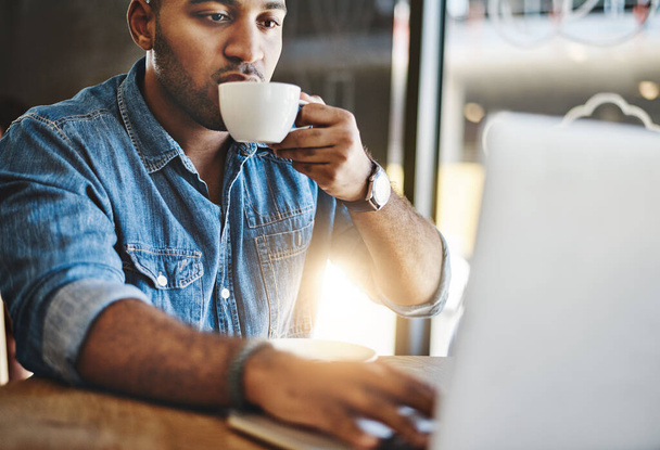 Kaffee hält ihn fokussiert. Aufnahme eines hübschen jungen Mannes, der Kaffee trinkt, während er in einem Café arbeitet. - Foto, Bild