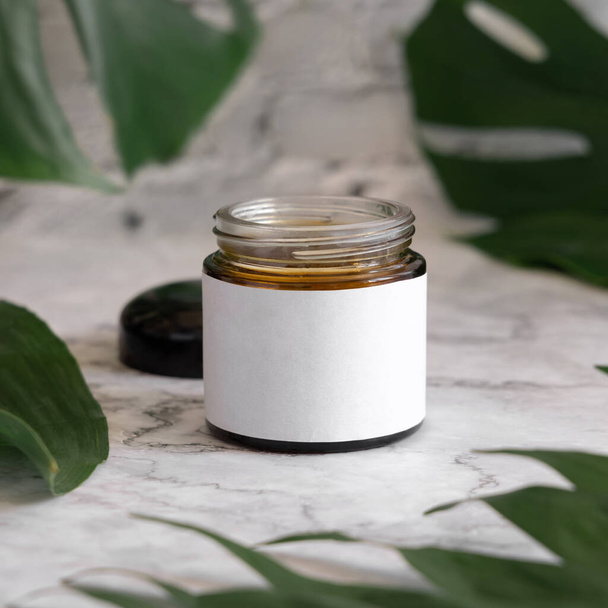 Opened Brown jar and monstera leaves on marble table close up. Brand packaging mockup. Skincare beauty product, cream or butter. Making homemade herbal cosmetics from natural ingredient - Foto, afbeelding